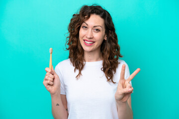Obraz premium Young caucasian woman brushing teeth isolated on blue background smiling and showing victory sign