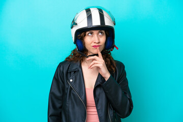 Young caucasian woman with a motorcycle helmet isolated on blue background having doubts while looking up