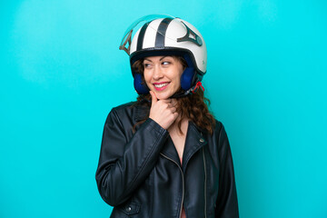Young caucasian woman with a motorcycle helmet isolated on blue background looking to the side and smiling