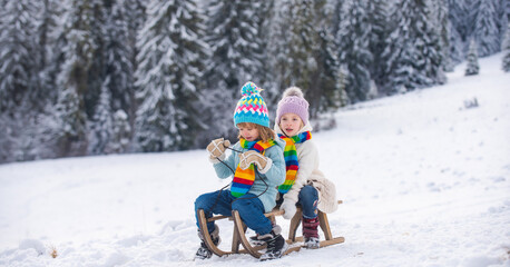 Happy little boy and girl sledding in winter. Kids sibling riding on snow slides in winter. Son and...