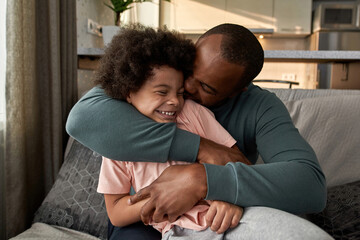 Father embracing joyful little son on sofa at home