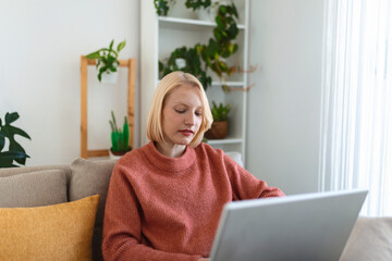 Smiling young woman using laptop at home, looking at screen, chatting, wearing wireless headset having video conference . business trainer tutoring by webcam, online training, e-coaching concept