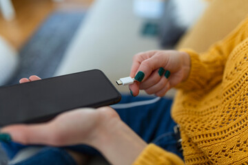 Woman hands plugging a charger in a smart phone. Woman using smartphone with powerbank, charging power to smart phone. Woman charging battery on mobile phone at home - obrazy, fototapety, plakaty
