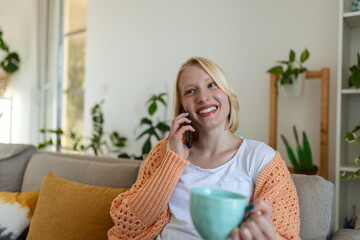 Attractive smiling woman using smart phone while sitting on the sofa at home. Communication and coziness concept.