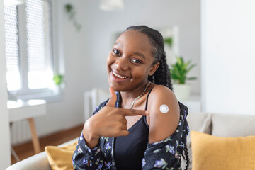 Portrait of a female smiling after getting a vaccine. Woman holding down her shirt sleeve and showing her arm with bandage after receiving vaccination.