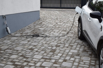 Charging white electric car from home power grid on backyard. Hybrid car Electric charger.
