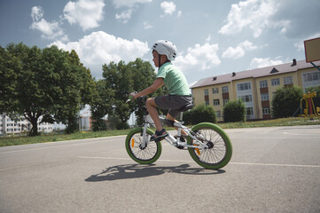 Fototapeta premium An active European child, a 9-year-old boy in protective gear for cyclists, in a sports helmet, rides a bicycle on an asphalt road on a sunny summer day. Active and healthy lifestyle concept