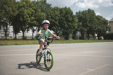 Naklejka premium Elementary age Caucasian boy, sporty active child in sports helmet, learns extreme tricks and extreme cycling in city, cycling on the asphalt road outdoors. Sport. Active, healthy lifestyle concept