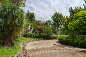 Beautiful curved stone path in the garden among trees and stones. Cloudy sky with rain clouds.