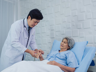 Obraz premium Happy smile beautiful Asian elderly old woman patient in light blue dress lying on bed while male doctor in white suit holding her hand and giving intravenous fluid on hand in the hospital room.