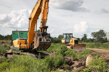 A caterpillar excavator digs the earth with a bucket, and a bulldozer clears the earth with a metal shield. Drainage of swamps. Peat mining. Clearing the construction site.