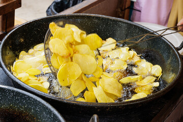 Frying sliced potatoes in oil and stirring with a slotted spoon