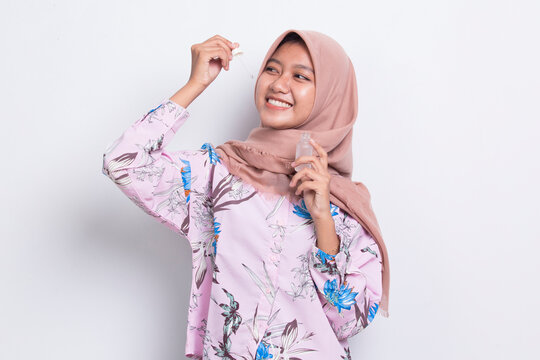 young beautiful asian muslim woman putting moisturizing serum to her face isolated on white background
