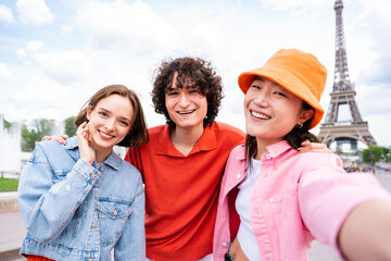 Multiethnic group of young happy teens friends bonding and having fun while visiting Eiffel Tower...