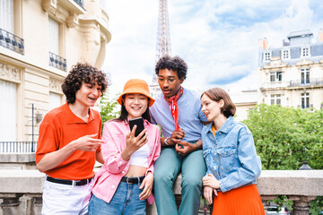 Multiethnic group of young happy teens friends bonding and having fun while visiting Eiffel Tower...