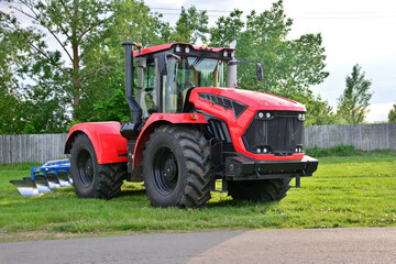 Obraz premium red and black tractor with plough isolated on green grass with fence on background