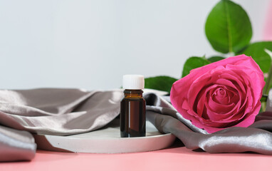 rose petals oil. essential oil for face care and skin moisturizing. a bottle of aroma oil and fresh pink rose on silk sheet.