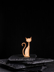 silhouette of a cat made of wood, a wooden cat sits on a black slate black background