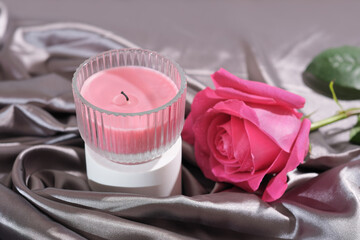 pink rose and soy wax candle on silk satin draped bedding sheet. romantic date, celebration or proposal evening.