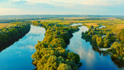 Aerial view above a beautiful landscape with a  river while sunset. Aerial view from drone flies over a beautiful summer landscape.