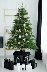 A stylish Christmas tree stands in the living room. Gifts in black and white under the Christmas tree