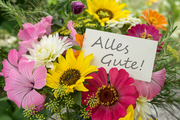Colorful bouquet of summer flowers with a greetings card and German text: All the best 