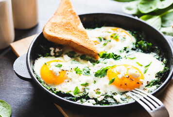 green shakshuka in a cast iron skillet. fried eggs with spinach and fried toast. healthy nutritious breakfast