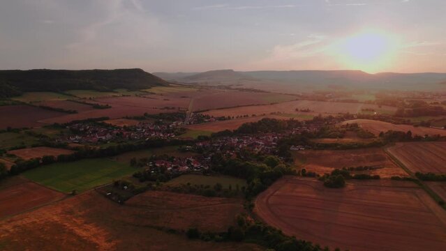 Aer ial view of a German village surrounded by meadows, farmland and forest at sunset in Germany.