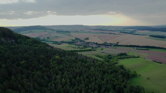 Aer ial view of a German village surrounded by meadows, farmland and forest at sunset in Germany.