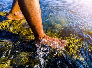 The feet of an asian man standing on a large mossy rock in the sea