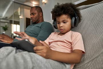 Fototapeta premium Boy use digital tablet while father type on laptop