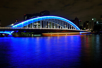 ブルーにライトアップされた永代橋をくぐる屋形船の眩い軌跡