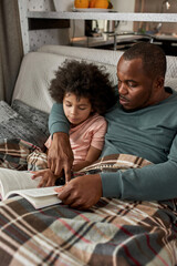 Father and son reading book on sofa under blanket