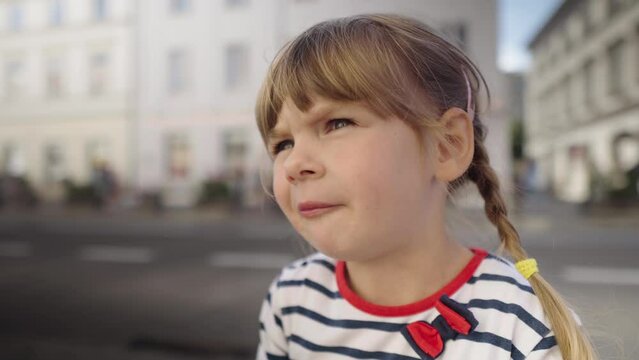 Little girl eating tasteless jelly candy on the street. Child first tastes harmful sweets. Unhealthy food. Portrait of a kid who eats. 