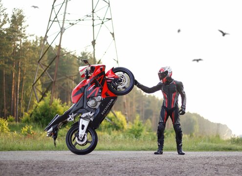 KRASNOYARSK, RUSSIA - April 23, 2019: Beautiful motorcyclist in full gear and helmet on a red and black Honda 2005 CBR 600 RR (PC37). Lifted the bike over the front wheel