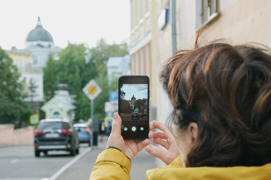 Elderly brunette woman takes pictures of an Orthodox church on a smartphone. Tourist woman photographs a landmark while walking around the city.