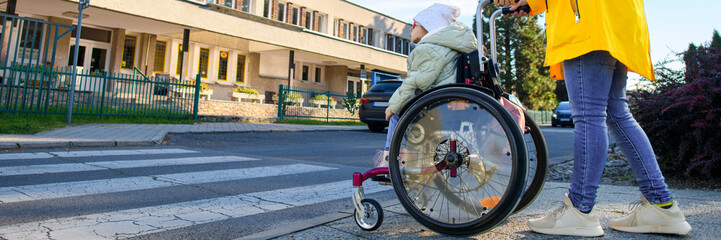 Mother pushing wheelchair with her daughter, young girl living with cerebral palsy, on their way to therapy. Cerebral palsy is lifelong condition that affects movement and co-ordination.