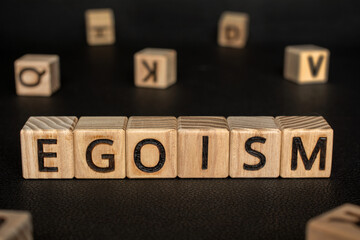 Egoism - word from wooden blocks with letters, an undue sense of self-importance concept, random letters around black Leather background - obrazy, fototapety, plakaty