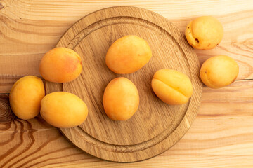 Several ripe yellow pineapple apricots on a wooden tray, close-up, on a wooden table, top view.