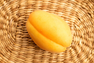 One yellow pineapple apricot, macro, on a straw mat, top view.