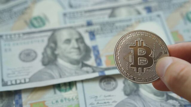 Man hand holding crypto currency silver Bitcoin coin above dollars background