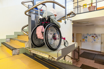 Young child living with cerebral palsy using electric wheelchair lift to access public building....