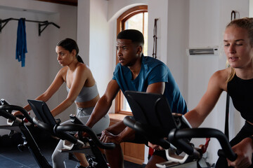 Fototapeta na wymiar Group of resilient young multiracial adults doing cardio on exercise bike at the gym