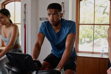 Determined young black man and biracial woman doing cardio exercise bike at the gym