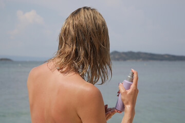 Woman applying sunscreen spray, hair care protection during summer vacation	