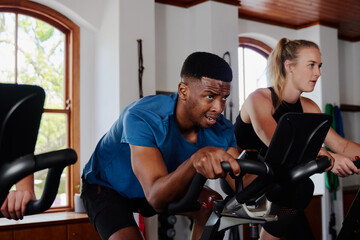 Fototapeta na wymiar Determined young black man and caucasian woman doing cardio on exercise bike at the gym