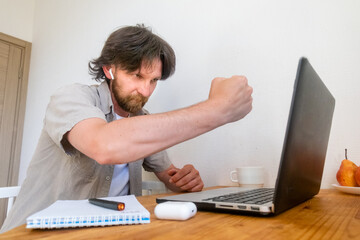 Angry bearded man with a laptop in his ear shakes his fist at the laptop screen