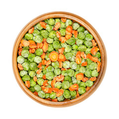 Dehydrated green peas and carrot pieces in a wooden bowl. Mixed vegetables. Seeds of pod fruit Pisum sativum, and cut orange carrots, Daucus carota, a root vegetable. Closeup, from above, food photo.