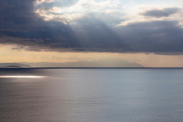 Early morning view of the sunrise over the Mediterranean Aegean Sea. View on the peninsula Mount Athos (Again Oros), Chalkidiki, Central Macedonia, Greece, Europe. Sun beams on the water surface, calm