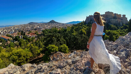 Rear view of tourist woman wearing a white dress and golden laurel crown looking at Parthenon of...